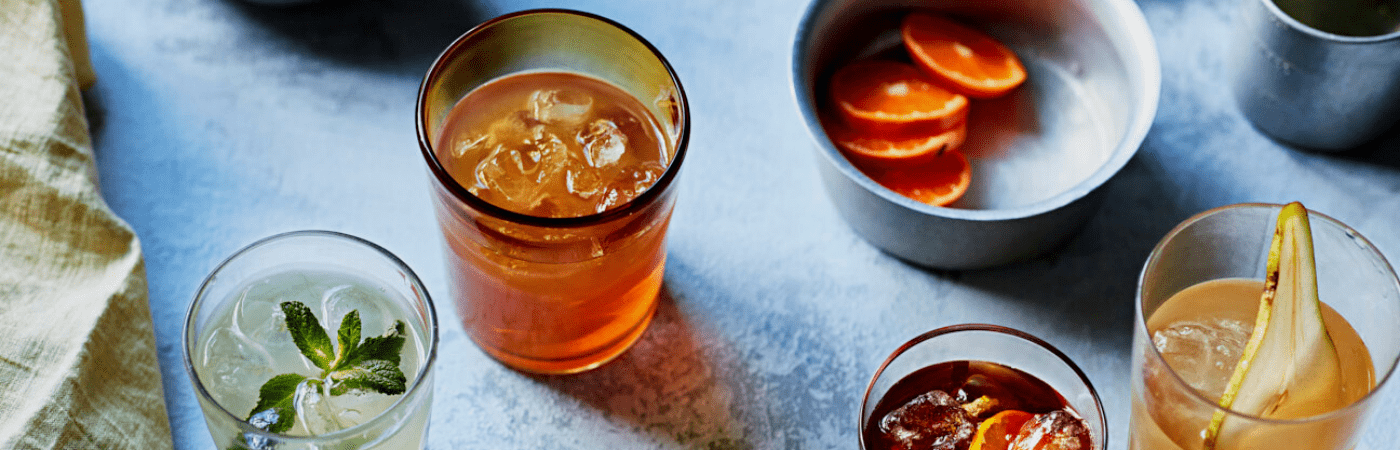 A selection of iced tea cocktails on a table alongside a bowl of sliced fruit