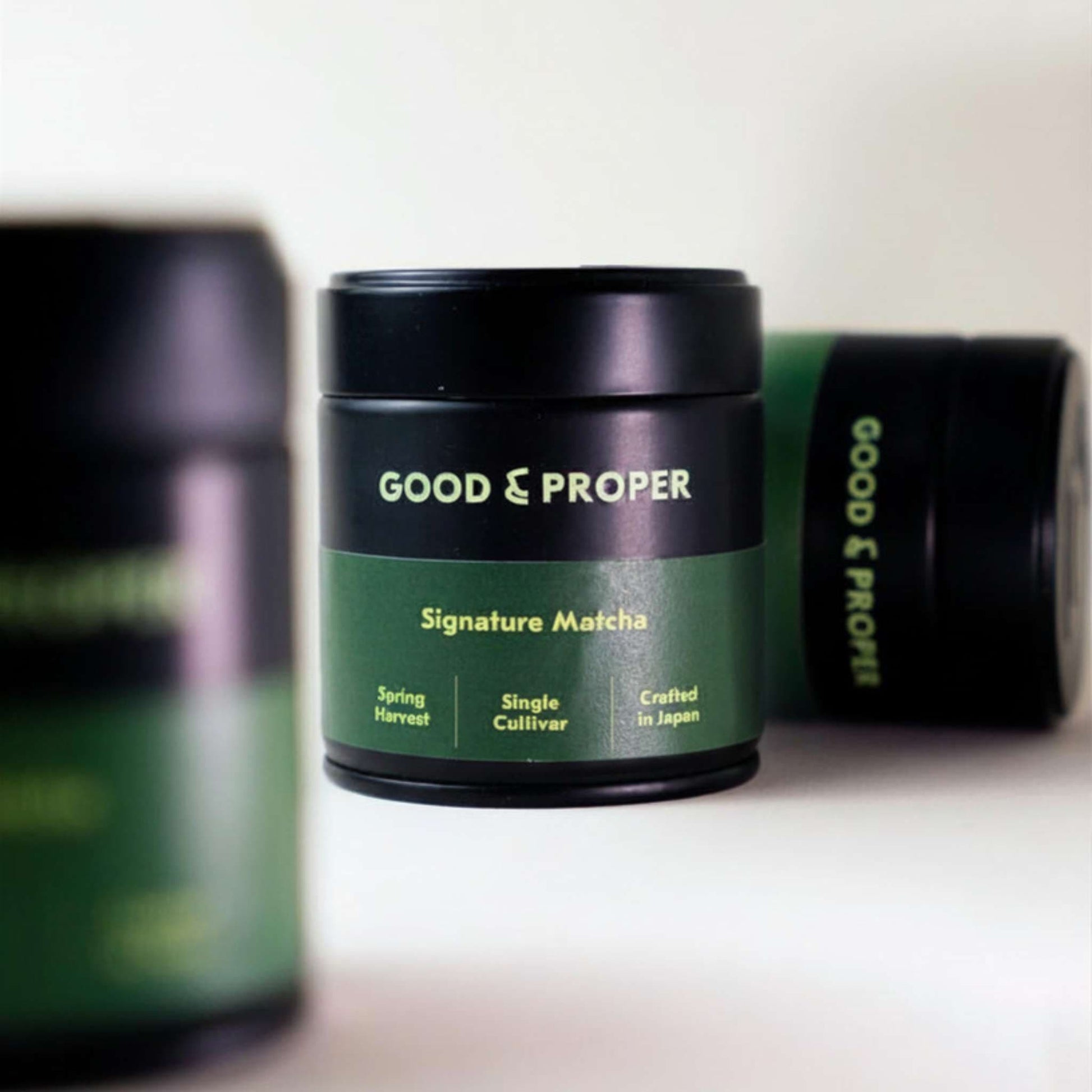 Green and black containers of Good & Proper Signature Matcha (powdered green tea) on a white surface
