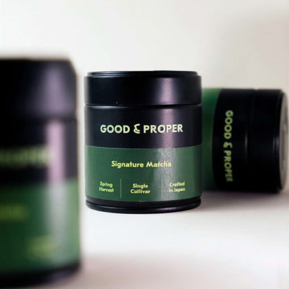Green and black containers of Good & Proper Signature Matcha (powdered green tea) on a white surface