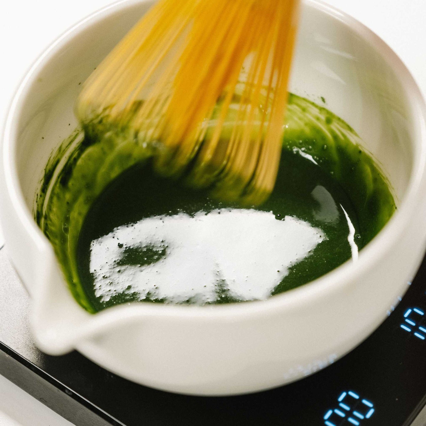 Matcha Green tea powder from Good & Proper Tea being whisked with hot water in a white matcha bowl on a black scale